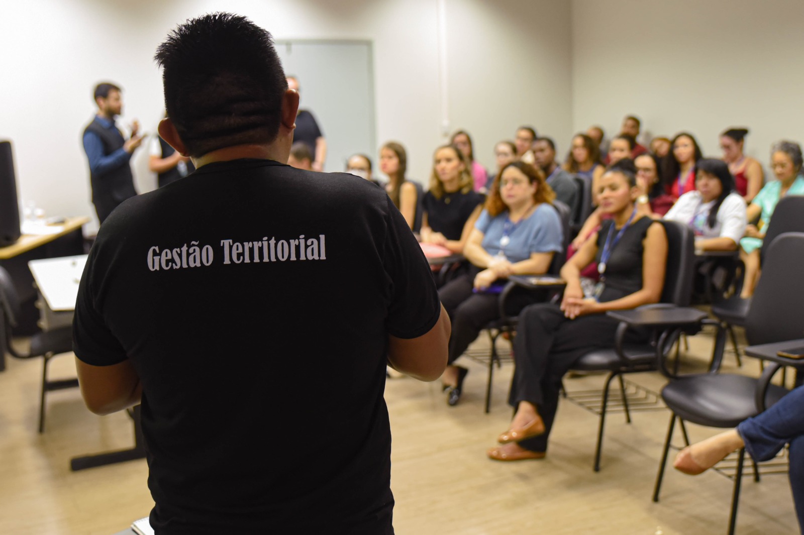 foto colorida tirada pelas costas do Dário Vitório Kopenawa Yanomami e ao fundo pessoas sentadas