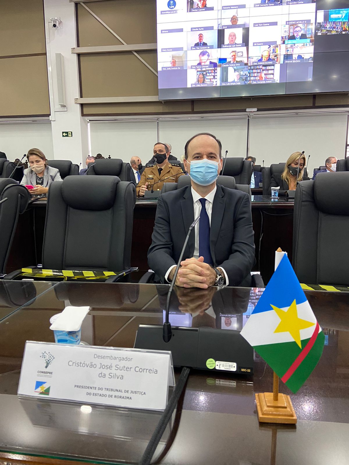 Imagem colorida mostrando o presidente, desembargador Cristóvão Suter, participando da posse da Diretoria do Conselho de Presidente dos Tribunais de Justiça, na mesa, uma bandeira do Estado de Roraima