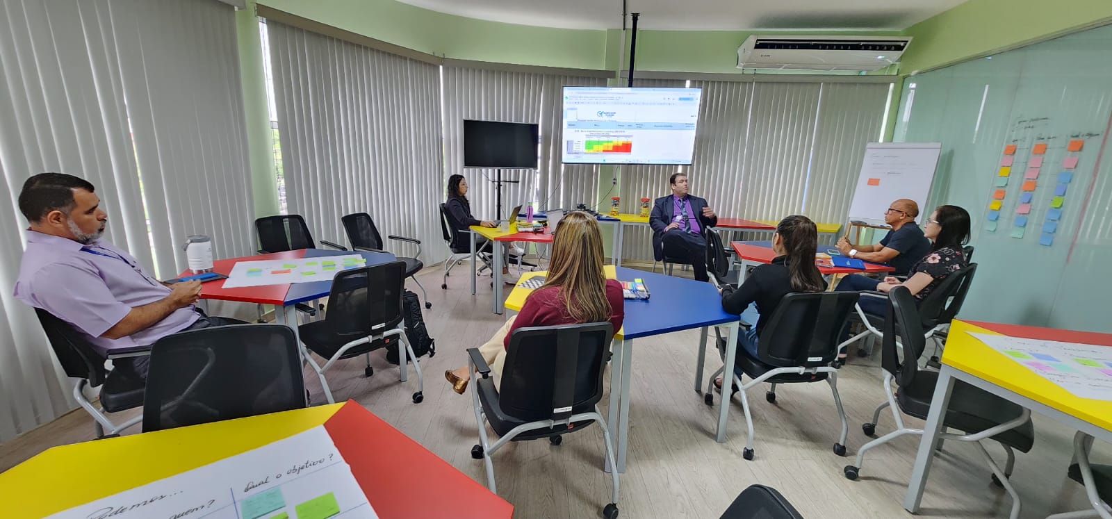 Foto colorida mostrando pessoas sentadas durante reunião 