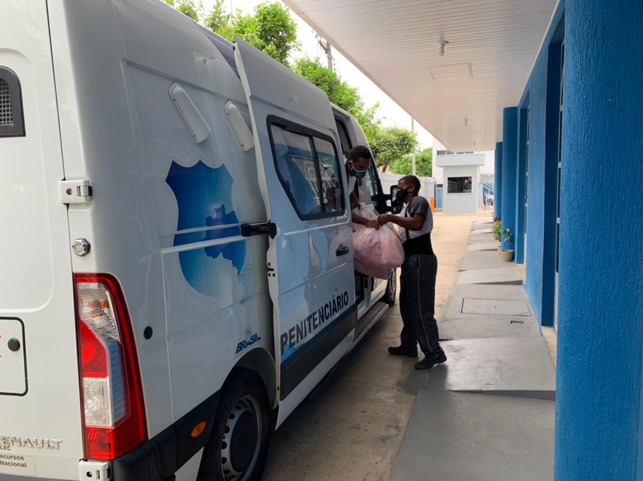 Foto da van com uniformes parada com um homem dentro dela e outro fora tirando as sacolas com uniformes.