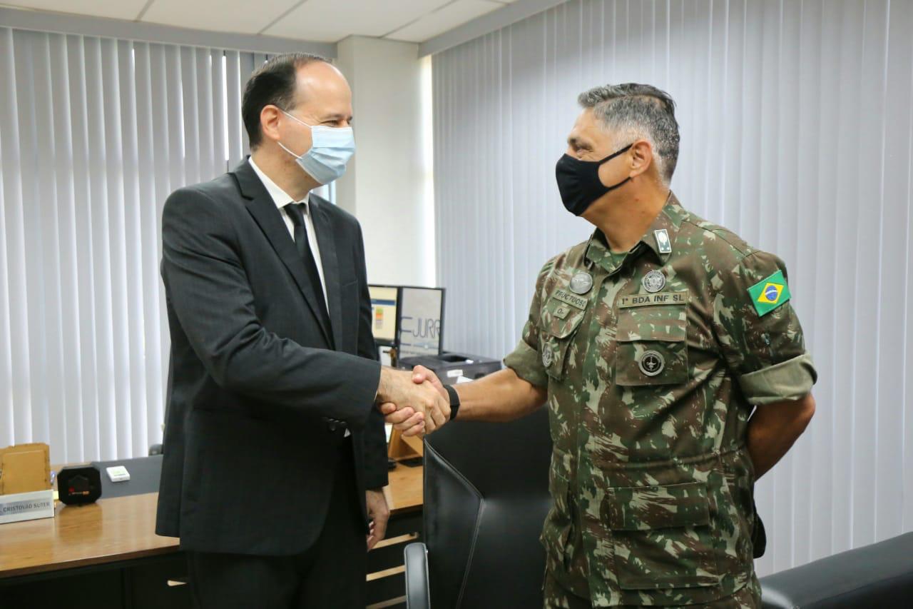 Foto do Presidente do Tribunal de Justiça de Roraima, desembargador Cristóvão Suter; e do comandante da 1ª Brigada de Infantaria de Selva, General Adriano Fructuoso da Costa; de pé se cumprimentando dentro de um escritório.