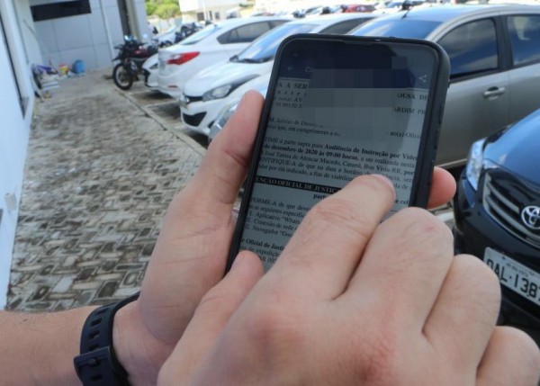 Foto de mão segurando um celular, com vários carros e uma moto estacionados em um estacionamento.