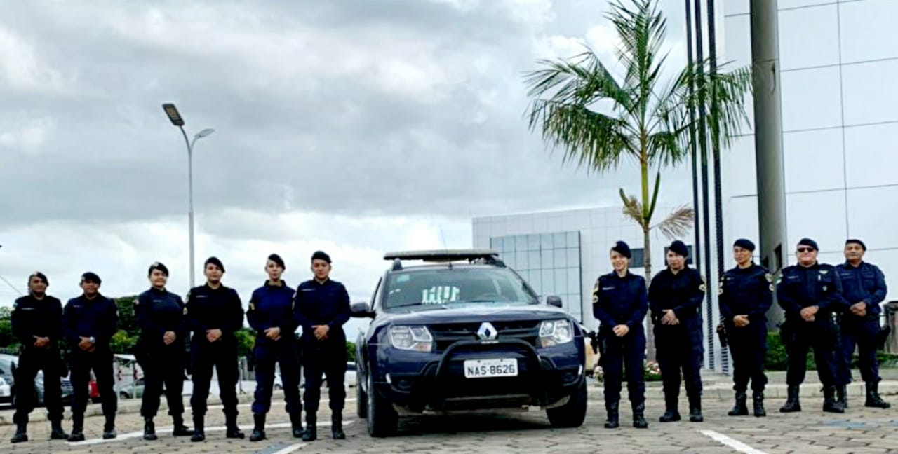 Foto de guardas municipais em pé ao lado de viatura da Patrulha Maria da Penha, seis do lado esquerdo e cinco do lado direito; em frente ao prédio do Fórum Criminal.