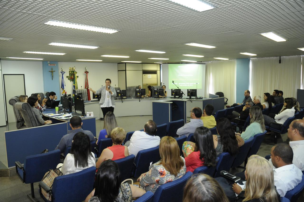 Foto de desembargadora falando para pessoas sentadas em cadeiras em auditório na frente dela e com bancada atrás dela.