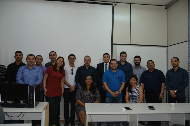 Servidores posando para foto em uma sala, com duas mesas na frente deles e um quadro branco atrás.