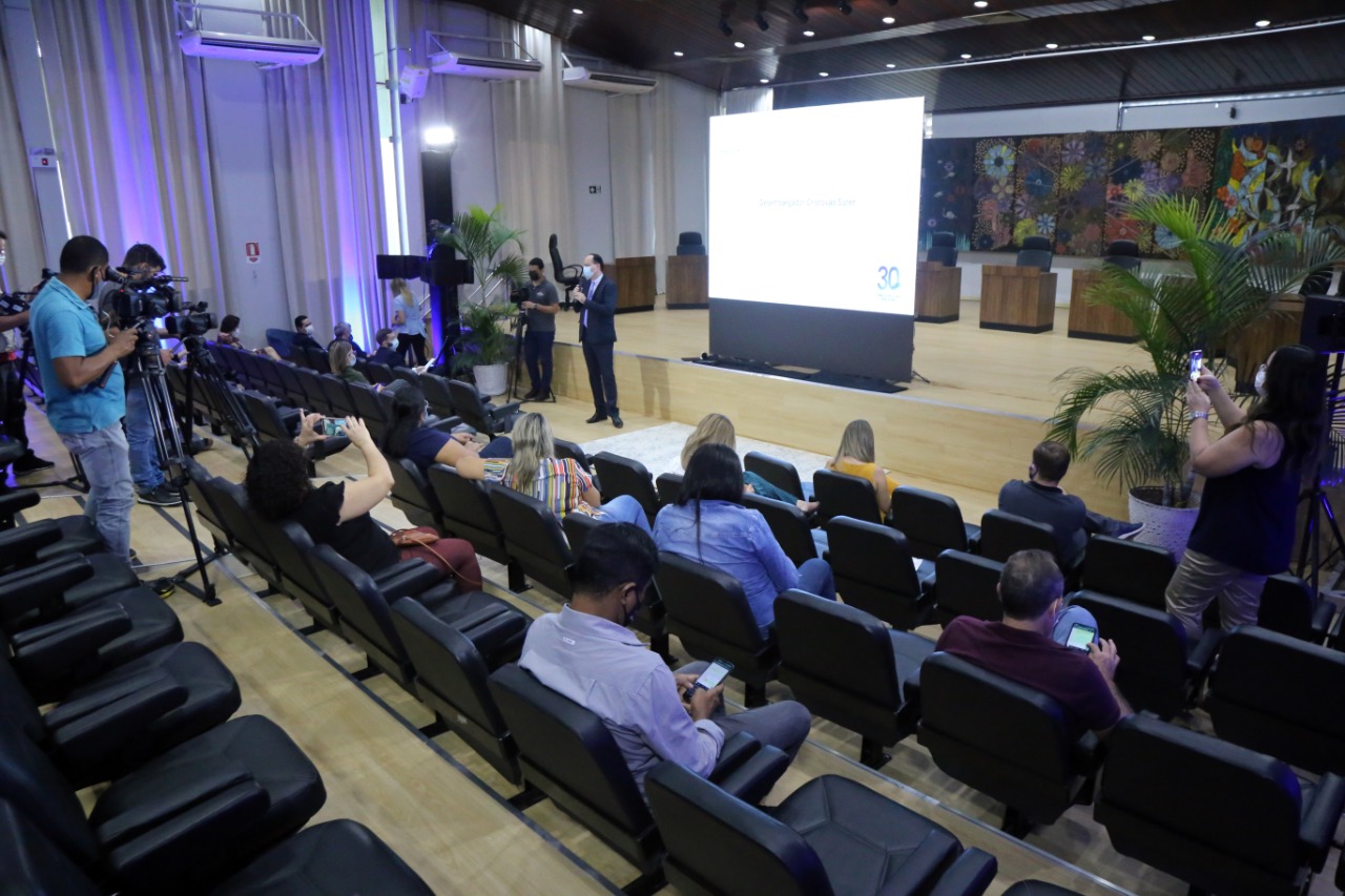 Foto de auditório, com pessoas sentadas em cadeiras, um cinegrafista filmando e ao fundo o Presidente do Tribunal de Justiça falando e uma apresentação sendo projetada.