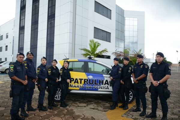 Nove guardas municipais de pé em frente a uma viatura da Patrulha Maria da Penha, ao fundo o prédio do Fórum Criminal.