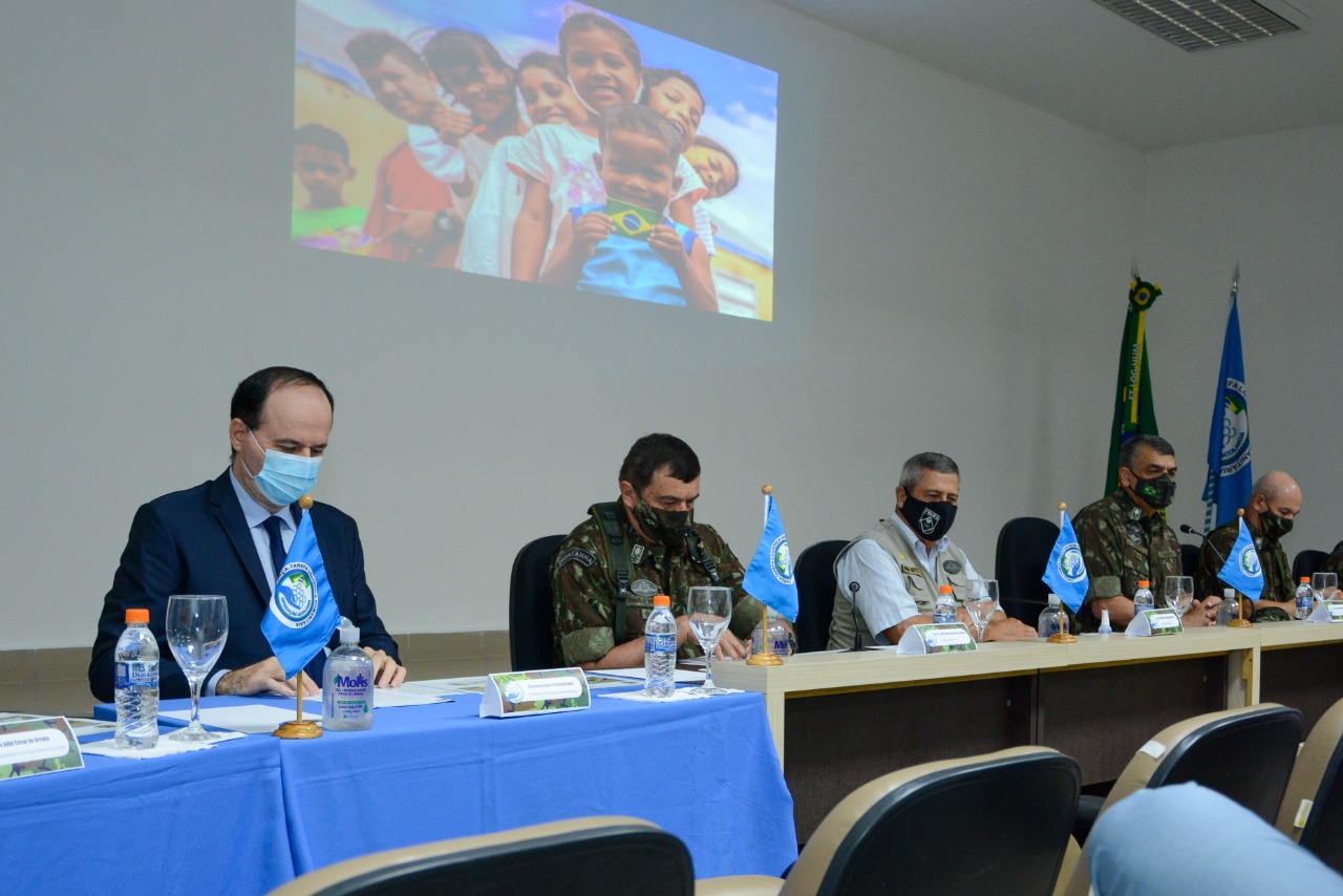 Presidente do Tribunal de Justiça, Ministro da Defesa e representantes do Exército sentados atrás da mesa do evento, com imagens de crianças projetada na parede atrás deles.