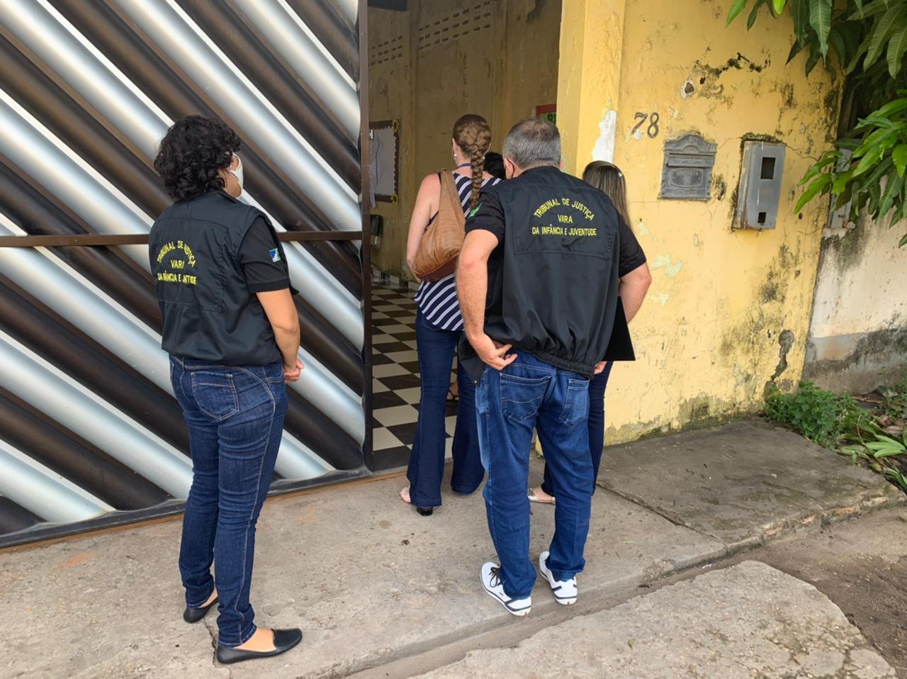 Servidores da Divisão de Proteção, em pé de costas em frente ao portão do abrigo feminino de Boa Vista.