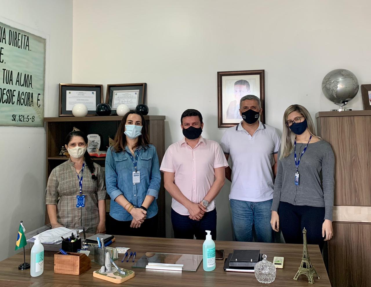 Cinco servidores do Tribunal de Justiça de pé, posando para foto, atrás de uma mesa em uma sala com dois armários e quadros na parede.