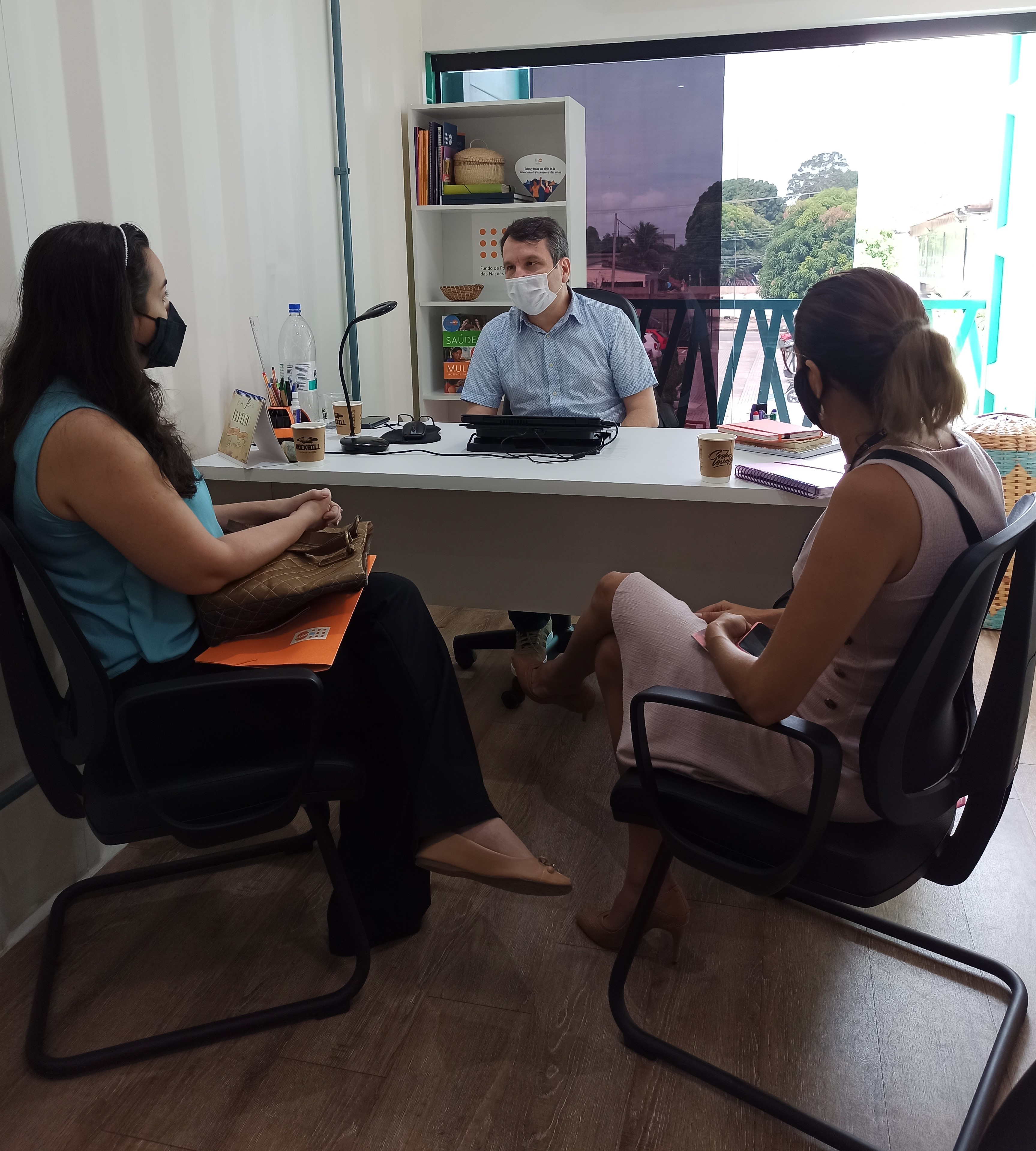 Duas servidoras sentadas em frente ao chefe de escritório do Unfpa, Igo Martini que está sentado atrás de uma mesa em uma sala.