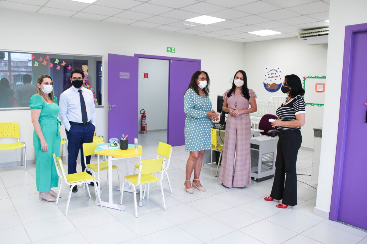 Servidores e representantes do Tribunal de Justiça de pé na sala da Casa da Mulher Brasileira, com mesinhas e cadeiras amarelas no meio da sala.