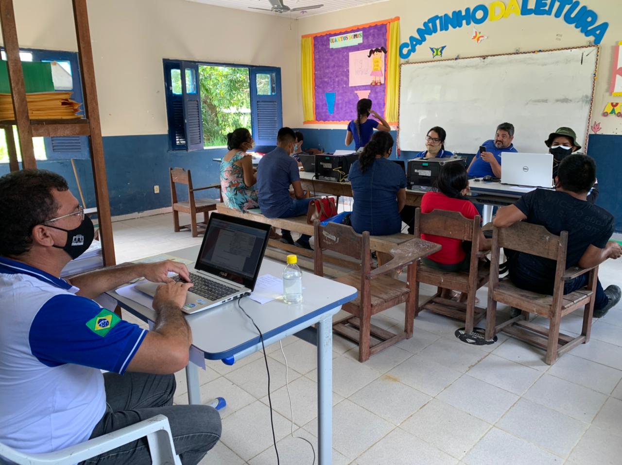 Servidores do Tribunal de Justiça de Roraima sentados em frente aos notebooks atendendo pessoas sentadas em cadeiras em uma sala decorada de escola infantil. 