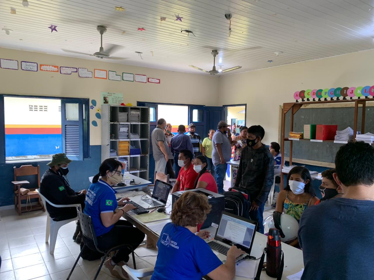 Servidores do Tribunal de Justiça de Roraima sentados em frente aos notebooks atendendo pessoas sentadas em frente as mesas e outras pessoas de pé esperando o atendimento.