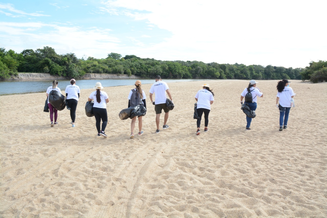 Pessoas andando de costas com sacos de lixo na mão 