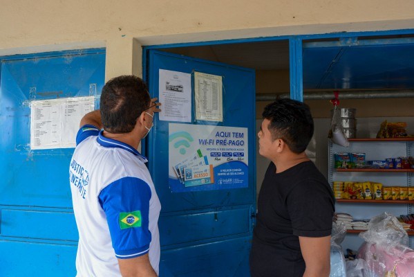 Servidor da Justiça Itinerante mostrando papel colado em uma porta de um mercadinho para morador de Pacaraima.