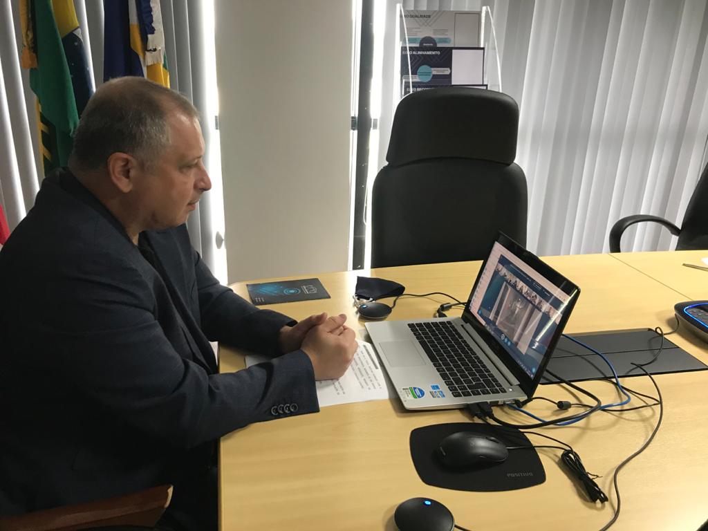 Desembargador Mozarildo Cavalcanti, sentado em uma sala, em frente de um mesa com notebook em cima, participando da solenidade virtual.