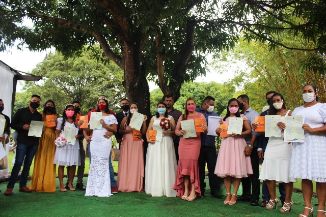 Casais do casamento coletivo de pé mostrando suas certidões de casamento.