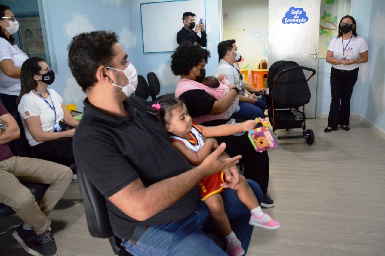 Na imagem contém servidores e servidoras, sentados com seus filhos e filhas durante apresentação das atividades do programa Primeiros Passos.