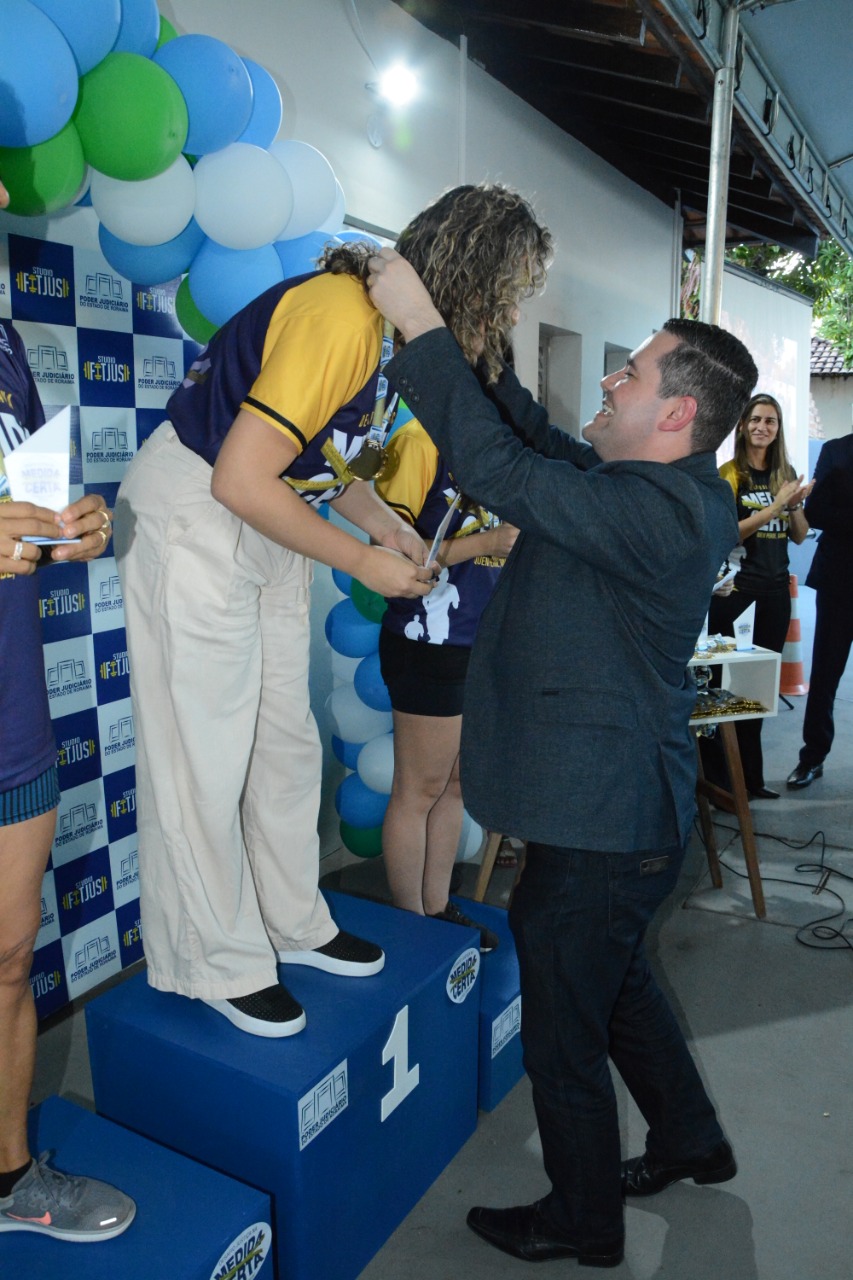 Foto colorida mostra secretário-geral, Felipe Queiroz, colocando medalha de primeiro lugar em participante da 2ª edição do Desafio Justiça na Medida Certa do TJRR. 