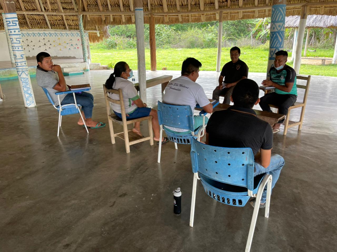 Imagem colorida contém seis indígenas sentados em cadeiras escolares de frente uns pros outros, debaixo de abrigo conhecido como tapiri, durante aula da nova turma de mediadores e conciliadores foi formada na Comunidade Maturuca, na Terra Indígena Raposa e Serra do Sol, localizada no município de Uiramutã, no extremo norte de Roraima.