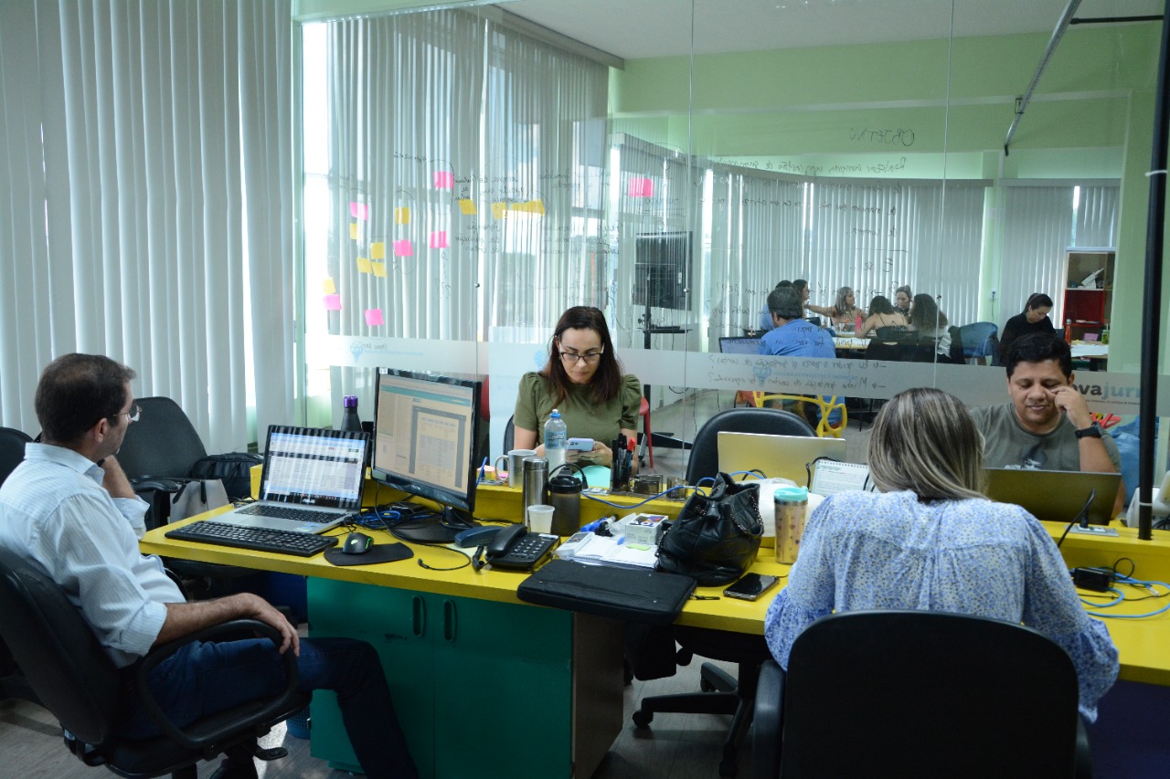 foto colorida mostra quatro pessoas sentadas frente a computadores, sendo dois homens e duas mulheres,na sala de inovação do TJRR.