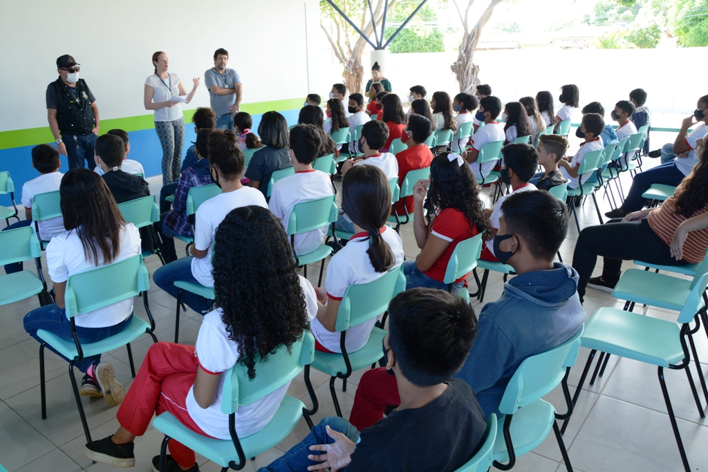 Imagem colorida contém equipe da Divisão de Proteção das  Varas da Infância e Juventude do Tribunal de Justiça de Roraima (TJRR), durante ação de conscientização do dia 18 de maio, dia nacional de Combate ao Abuso e à Exploração Sexual Contra Crianças e Adolescentes, ministrando palestra para vários alunos no pátio da escola 