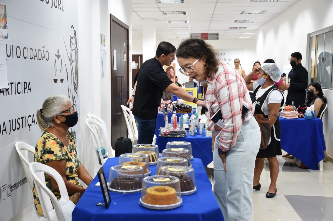 foto colorida contém a diretora do Fórum Criminal, juíza Lana Leitão, observando bolos durante a exposição.