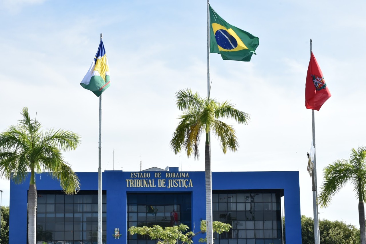 Imagem colorida do Palácio da Justiça contendo três bandeiras hasteadas, sendo elas a bandeira do Brasil, do Estado de Roraima e do Poder Judiciário de Roraima.