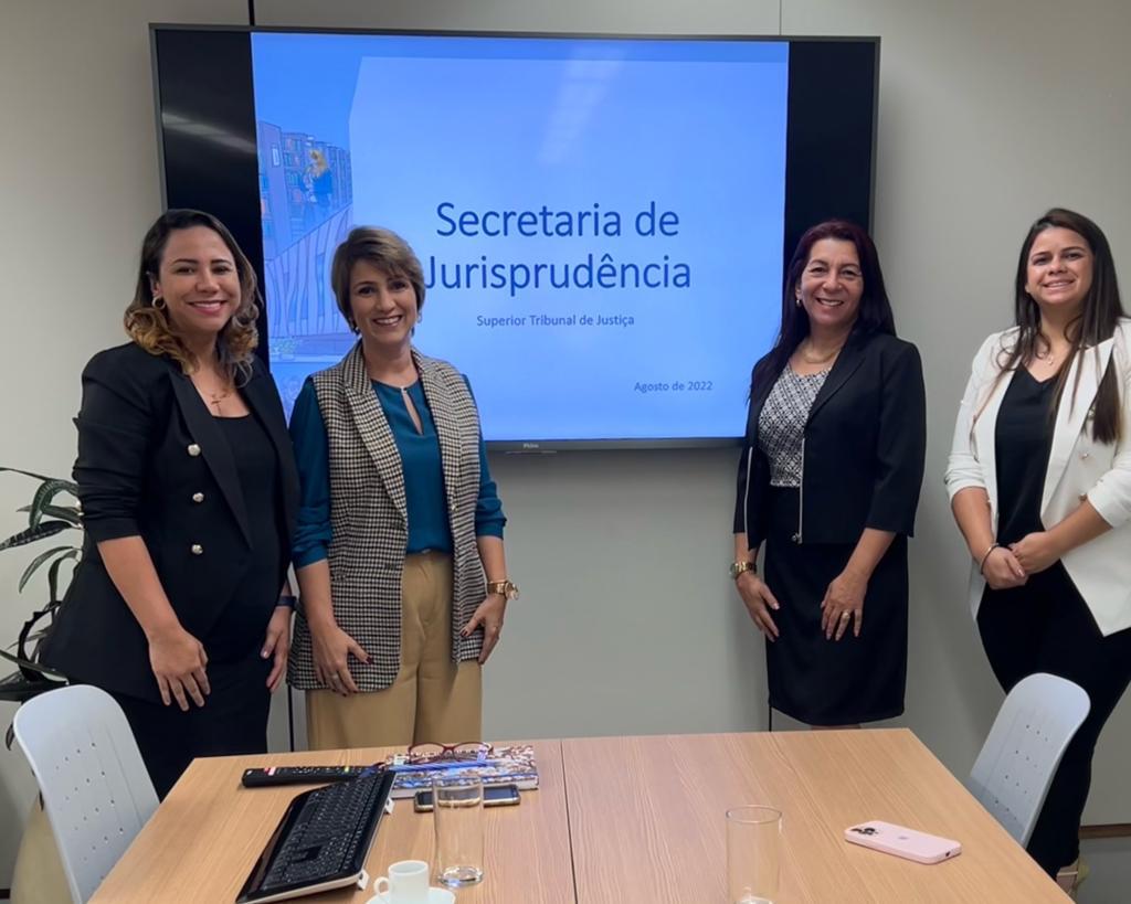 Imagem colorida mostra a Secretária de jurisprudência do STJ, Bárbara Brito com três servidoras do CPLJ, em uma sala com um monitor e uma mesa para reuniões.