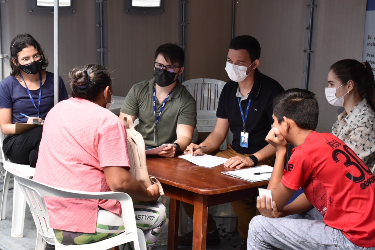 Imagem colorida contém seis pessoas reunidas conversando. Cinco delas usam máscaras. 