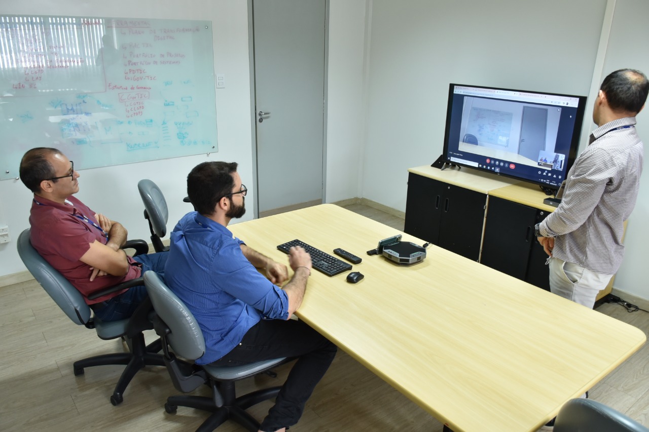 Imagem colorida contém o secretário de Tecnologia da Informação, Tiago Lobo, e mais dois servidores de frente para aparelho televisivo durante teste do sistema autônomo de internet. 