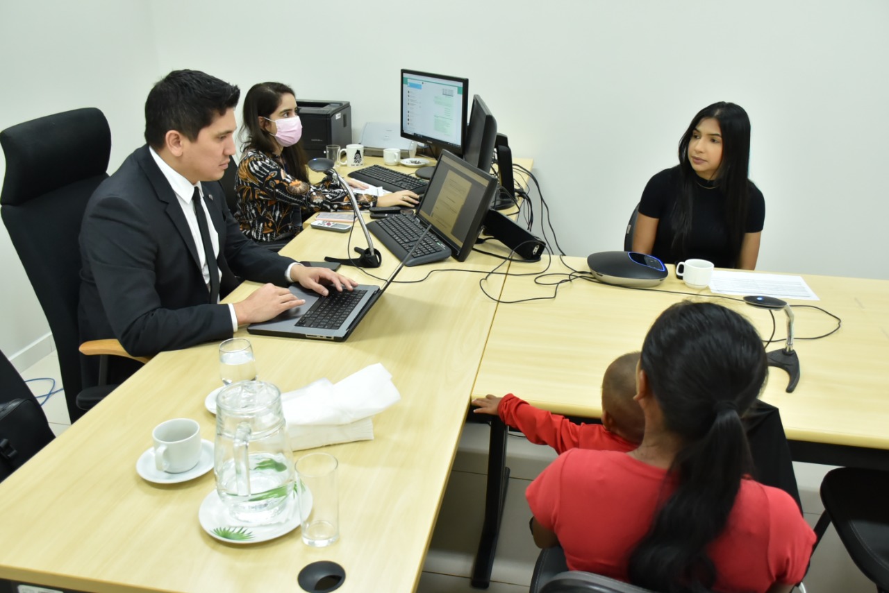 Imagem colorida contém o juiz da Coordenadoria da Infância e Juventude do Tribunal de Justiça de Roraima, Marcelo Lima de Oliveira e mais duas servidoras do TJRR, atendendo mulher e criança de colo. 