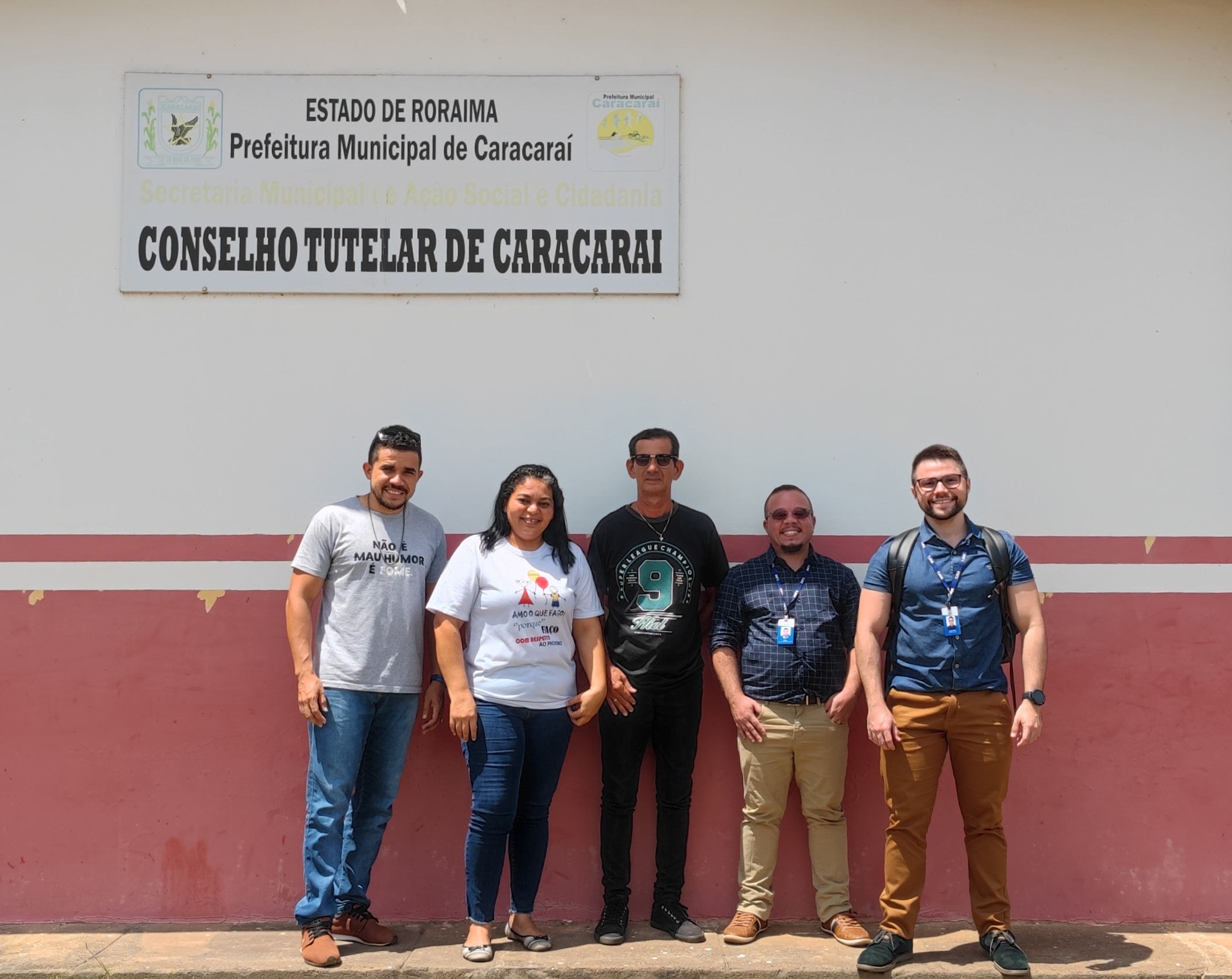 imagem colorida em formato quadrado mostra quatro homens e uma mulher em pé posando para  na frente da placa do conselho tutelar de Caracaraí. 