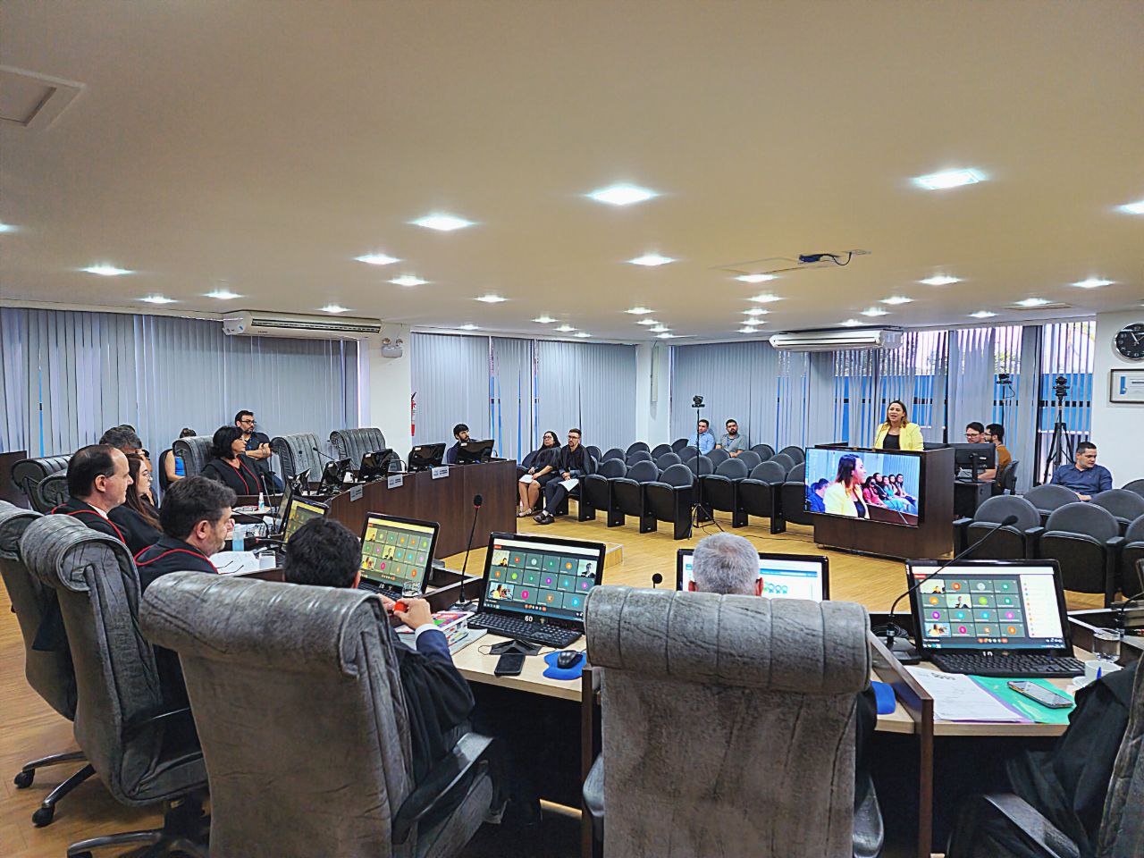 Imagem colorida mostra o presidente, Cristóvão Suter em uma sessão no pleno. Na sala há uma bancada em forma posicionada à frente de um pequeno auditório, sobre a bancada estão onze computadores  exibindo uma sala de reunião virtual. Na imagem aparecem 20 pessoas, sendo estes magistrados e magistradas, servidores e servidoras do Tribunal de Justiça.