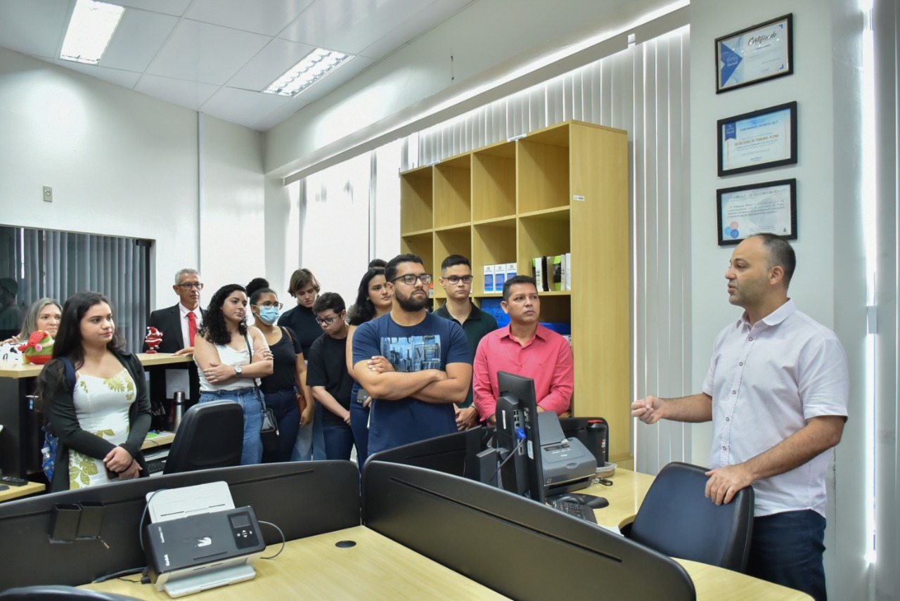  Imagem colorida em formato retangular, mostra os   acadêmicos de direito da Faculdade Cathedral visitando um dos departamentos do Tribunal de Justiça de Roraima .