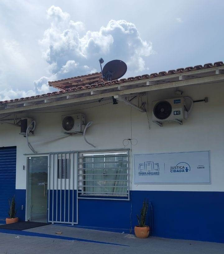 magem colorida em formato retangular, mostra a fachada do posto avançado do Programa Justiça Cidadã no município de Cantá, o prédio possui  janelas e portas de vidros com grades cinzas, e está pintada de branco na parte superior  e azul na parte inferior.