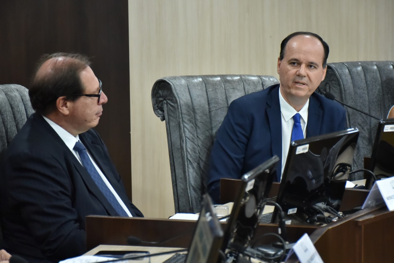  Imagem colorida em formato retangular,  mostra o presidente do Tribunal de Justiça de Roraima (TJRR), desembargador Cristóvão Suter e o corregedor-nacional de Justiça, ministro Luis Felipe Salomão, sentados em uma poltrona cinza atrás da bancada de sessão do pleno, estando o presidente falando no microfone, enquanto o ministro o observa. 