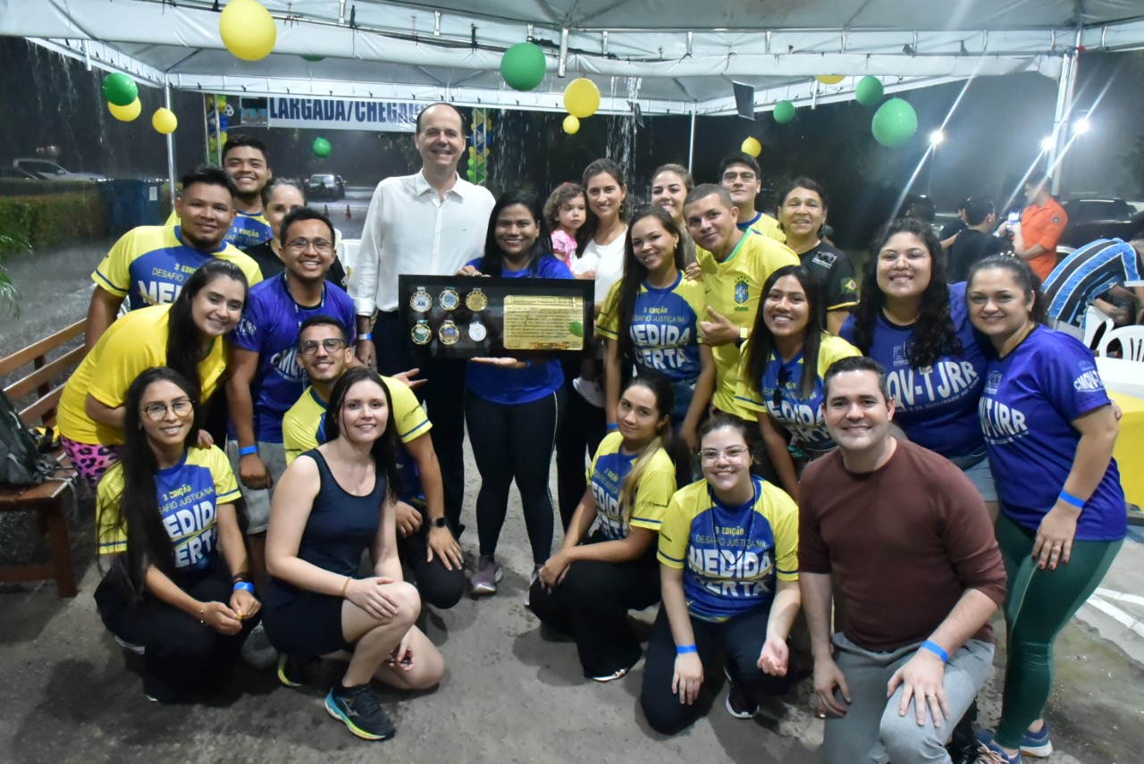 Imagem colorida em formato retangular, mostra o presidente do TJRR, desembargador Cristóvão Suter e o secretário-geral, Felipe Queiroz, com magistrados, magistradas, servidores e servidoras do Poder Judiciário de Roraima que fizeram parte das ações de saúde e integração, os participantes estão usando uma camisa azul com mangas amarelas identificadas com a frase medida certa.