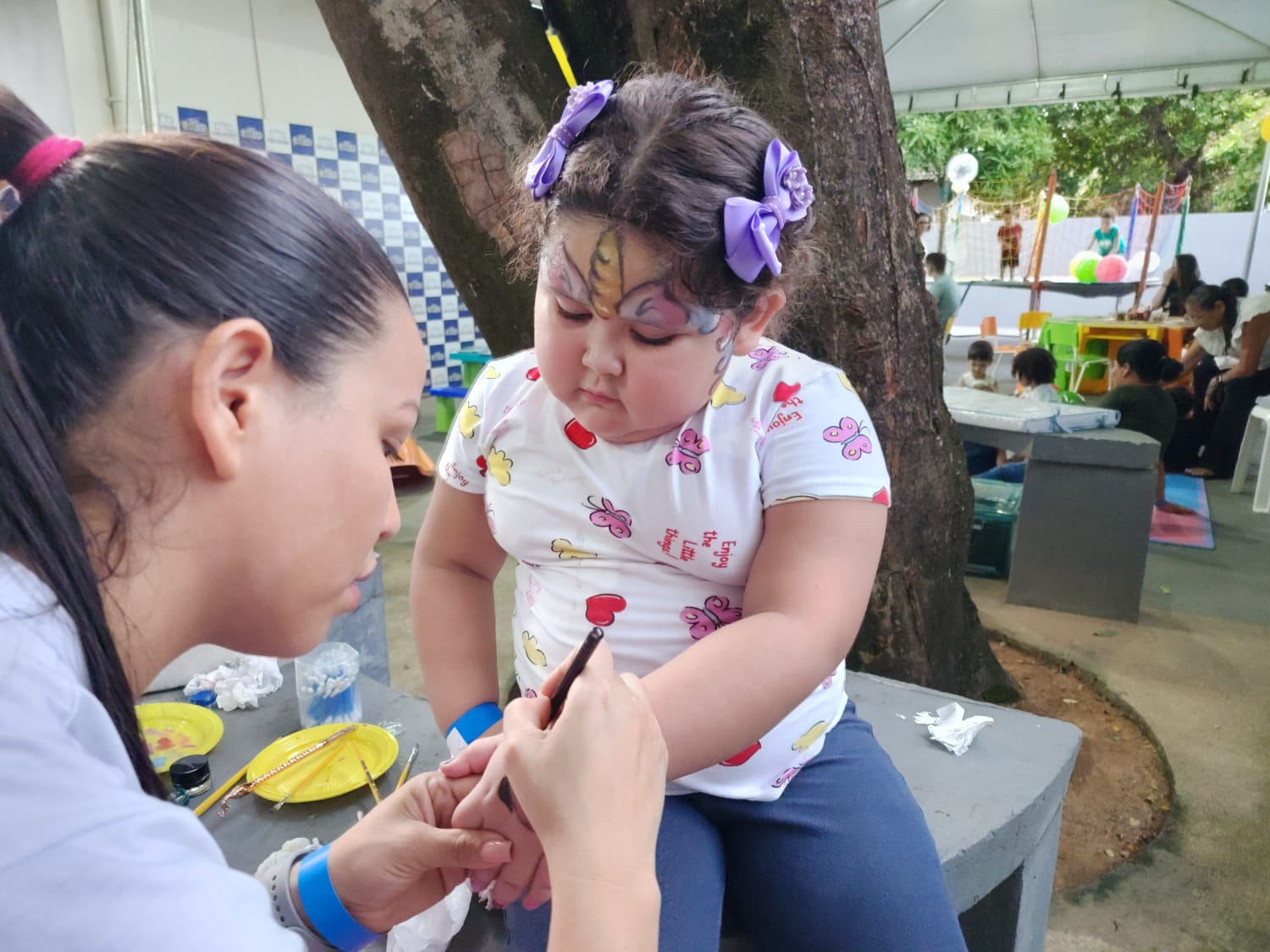  Imagem colorida mostra uma mulher realizando arte de pintura corporal em uma criança.