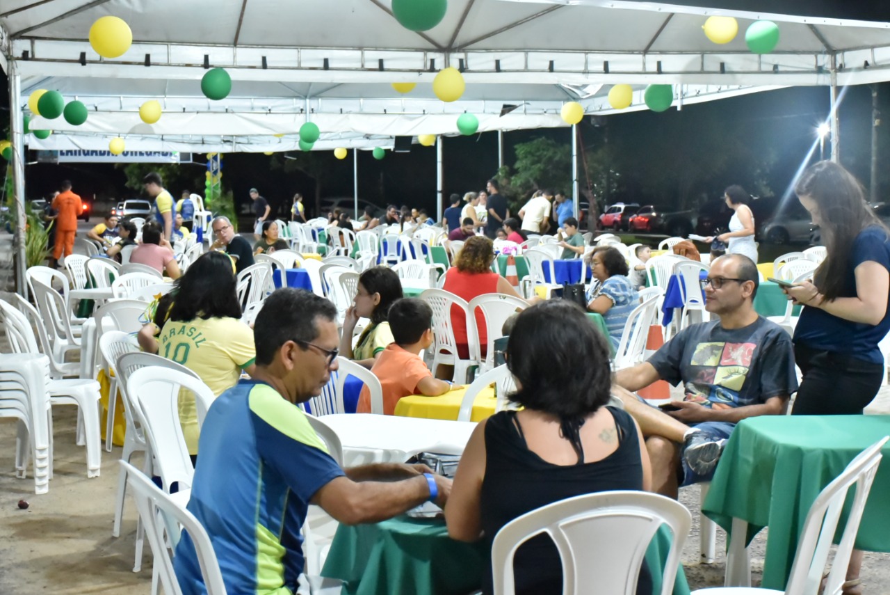 Imagem colorida mostra magistrados, magistradas, servidores e servidoras do Poder Judiciário de Roraima durante confraternização, o ambiente coberto foi decorado com as cores, verde, amarelo, azul e branco.