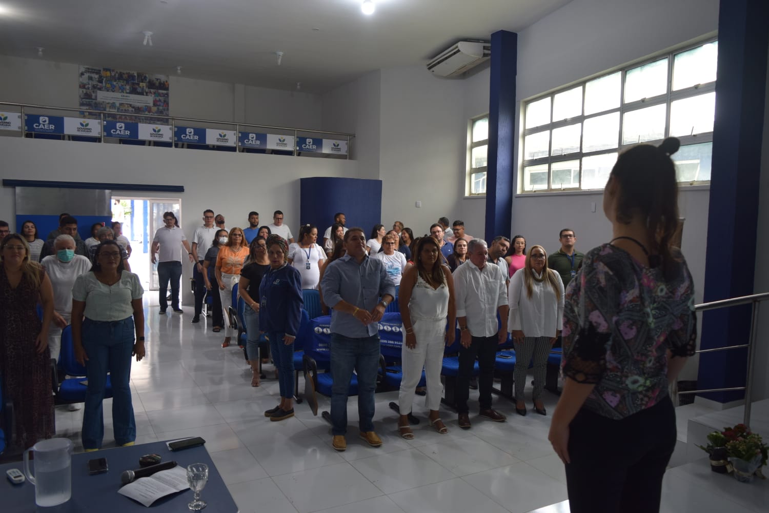 Imagem colorida em formato retangular mostra os colaboradores da Companhia de Águas e Esgotos de Roraima (Caer), durante uma sessão de meditação, à frente, mediando o evento está técnica judiciária Rudianna Zeidler.