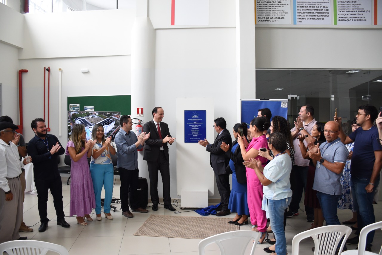 Imagem  colorida em formato retangular mostra o presidente do Tribunal de Justiça de Roraima, desembargador Cristóvão Suter, o vice presidente, Jésus Nascimento, comenta que o Tribunal de Justiça de Roraima, o secretário-Geral do Tribunal Felipe Queiroz, com magistrados e magistrados, servidores, servidoras, estagiários, estagiárias, terceirizados e terceirizadas  do o prédio Administrativo do Poder Judiciário, durante descerramento de placa de inauguração da usina de energia solar. instalada na unidade.