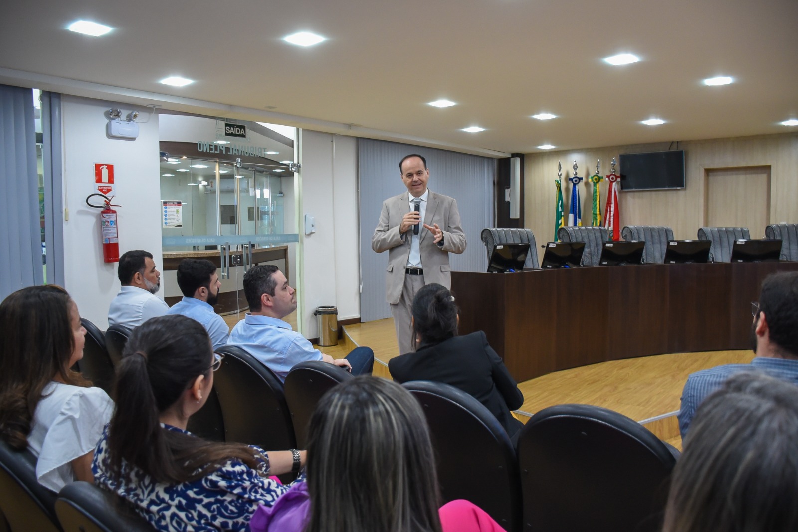 Imagem colorida em formato retangular mostra o presidente do Tribunal de Justiça de Roraima (TJRR), desembargador Cristóvão Suter, discursando em pé com o microfone na mão para secretários e coordenadores da instituição   que estão sentados no auditório da Sala de Sessões do Palácio da Justiça.