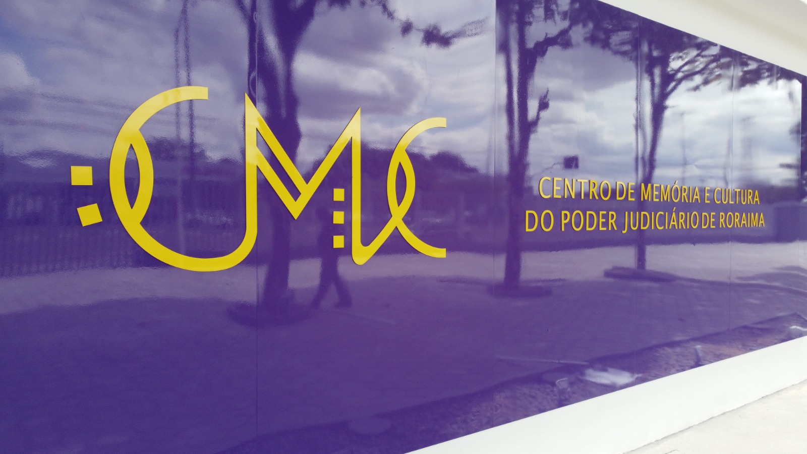 Imagem colorida em formato retangular mostra um painel na cor roxa com o logotipo “CMC” e ao lado a frase “Centro de Memória e Cultura do Poder Judiciário", ambas escritas na tonalidade amarela.