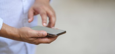 Foto mostra homem branco, com camisa branca, segurando um celular com uma mão e digitando com a outra.