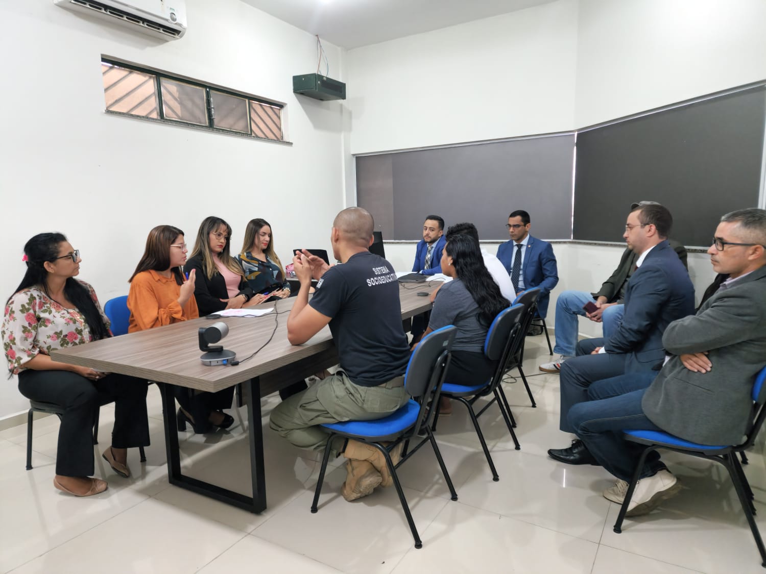 Imagem colorida em formato retangular mostra o juiz do Poder Judiciário Phillip Barbeiux sentado ao redor de mesa com a equipe técnica do CSE, psicólogos e assistentes sociais, Equipe Técnica das Varas da Infância e Juventude, representantes da Defensoria Pública do Estado de Roraima Ministério Público e representantes legais de socioeducandos.