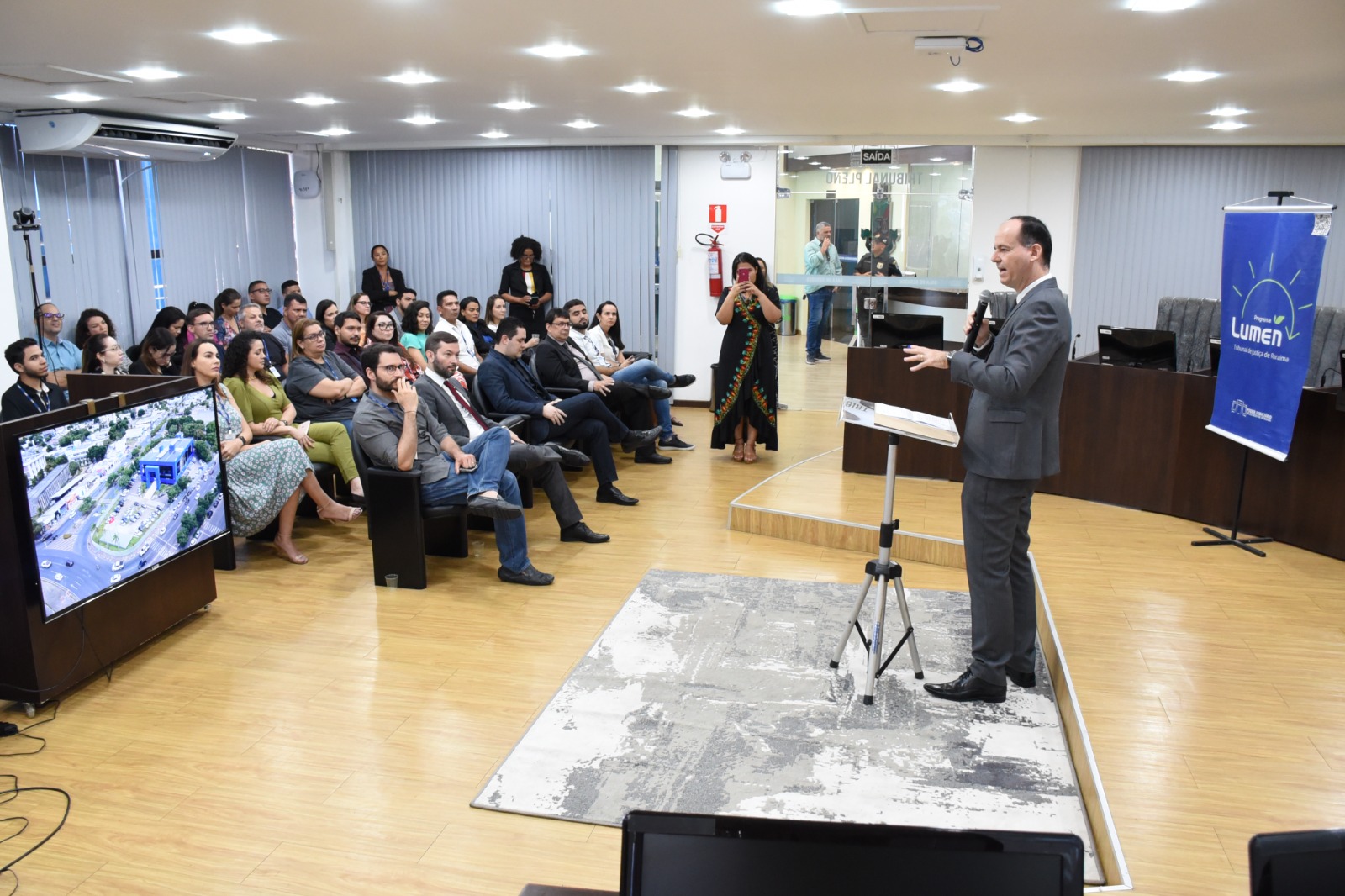 Imagem colorida em formato retangular mostra o presidente do Tribunal de Justiça de Roraima, desembargador Cristóvão Suter, em pé com o microfone na mão durante discurso para uma plateia composta por servidores, servidoras, magistrados e magistradas do Poder Judiciário.