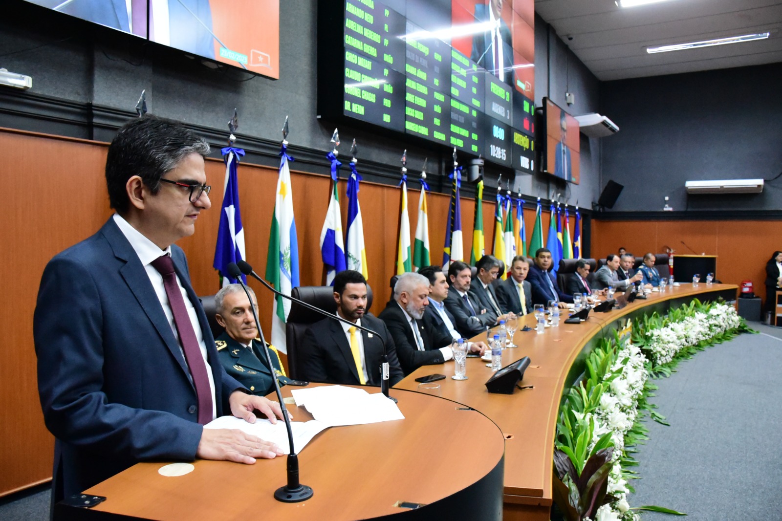 Imagem colorida mostra o desembargador Ricardo Oliveira, durante o discurso de solenidade de instalação da primeira sessão legislativa. Ao fundo  as autoridades sentaram-se à mesa de honra no Plenário da ALE-RR.