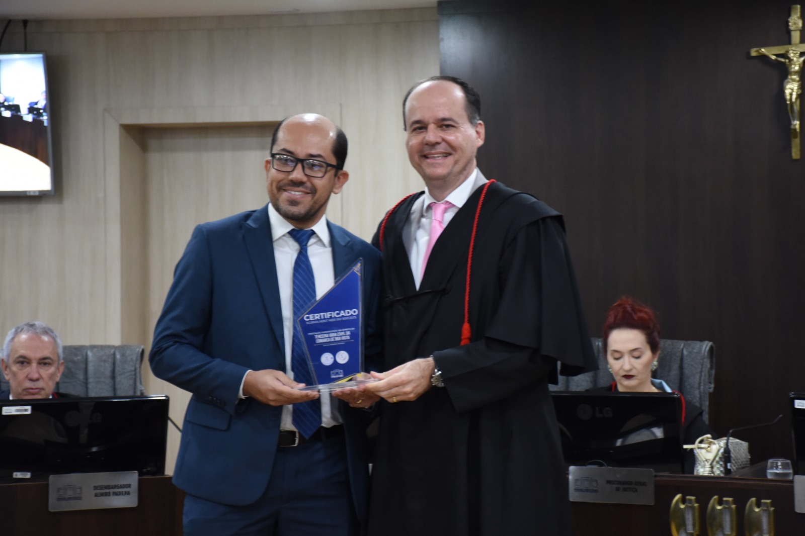 Imagem  colorida mostra o presidente do TJRR, desembargador Cristóvão Suter, posando para a foto ao lado de um servidor do Tribunal, ambos seguram o troféu certificado de qualidade de serviços prestados.